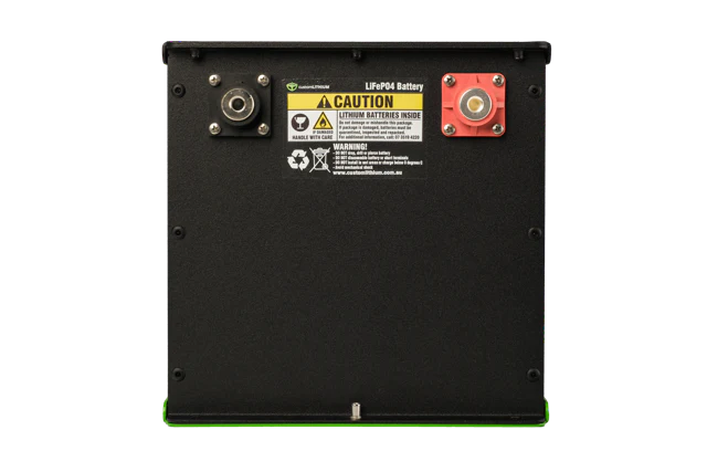 Rear face of a Custom Lithium LiFePO4 battery in a black aluminium enclosure, with a threaded negative terminal at the left, a red-shrouded positive at the right, and the caution label warning that lithium batteries are inside