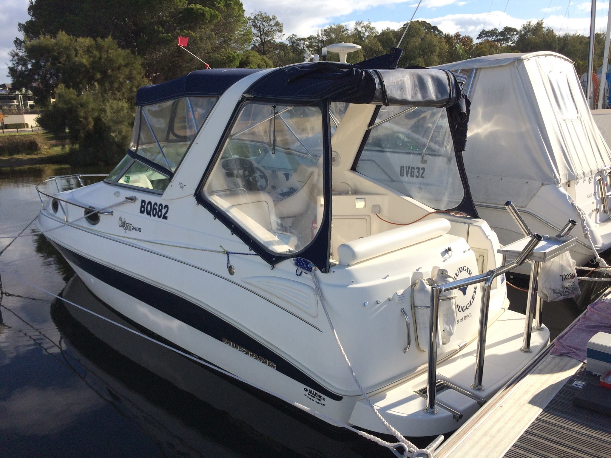 White boat with a black canopy on a dock with trees in the background