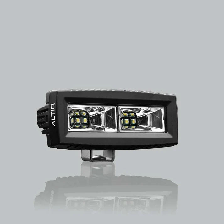 ALTIQ CX4 scene work light at a three-quarter angle, the wide rectangular lens holding two reflector segments each with a cluster of LEDs, the ALTIQ name on the end cheek and the mounting bracket below