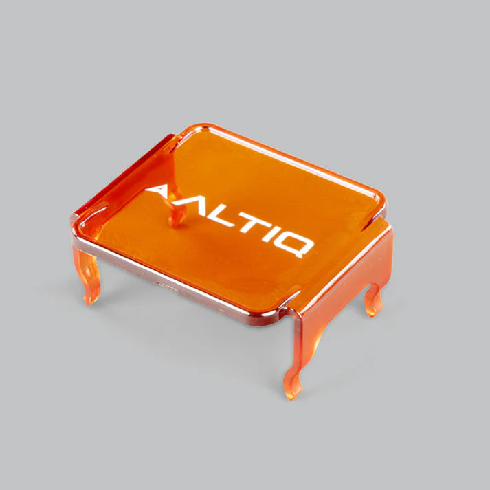 Amber ALTIQ DX4 lens cover seen from above at an angle, the translucent orange panel with the ALTIQ name across it and four moulded clips reaching down from the corners