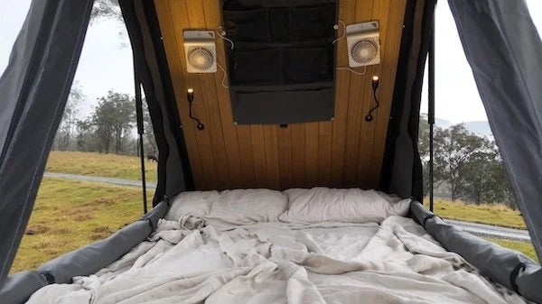 Bed inside a camper van with wooden paneling and curtains, outdoors.