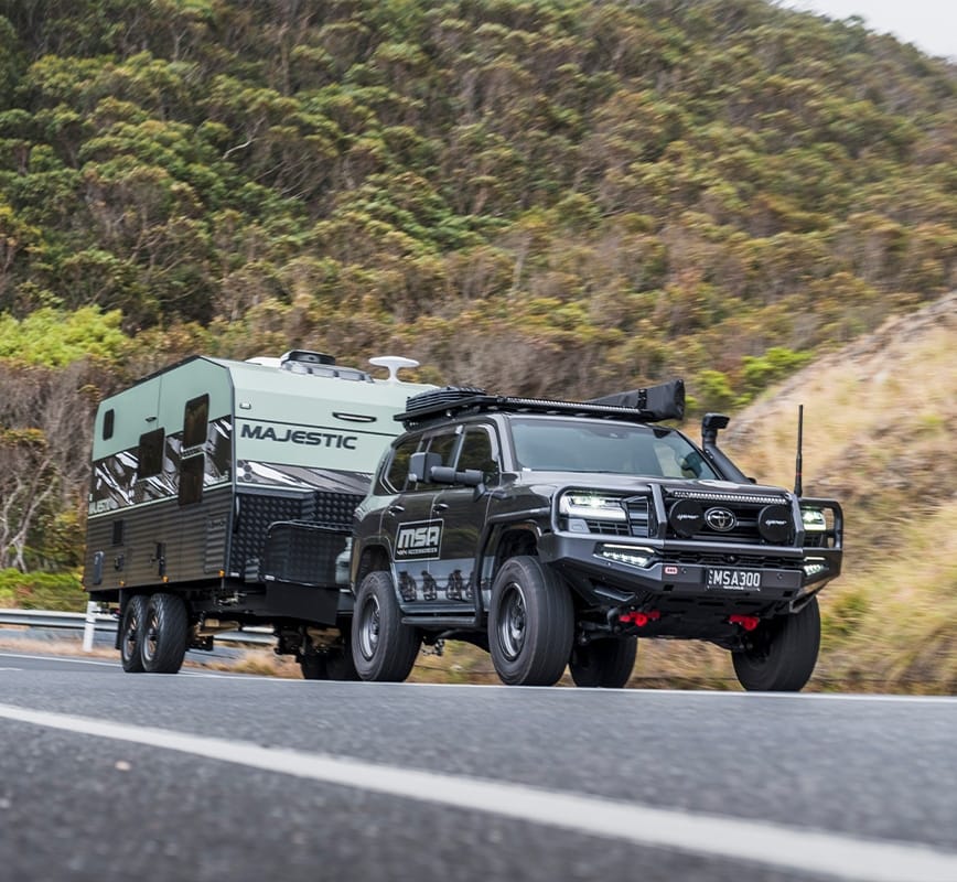Black SUV towing a green camper trailer on a road with a mountainous background