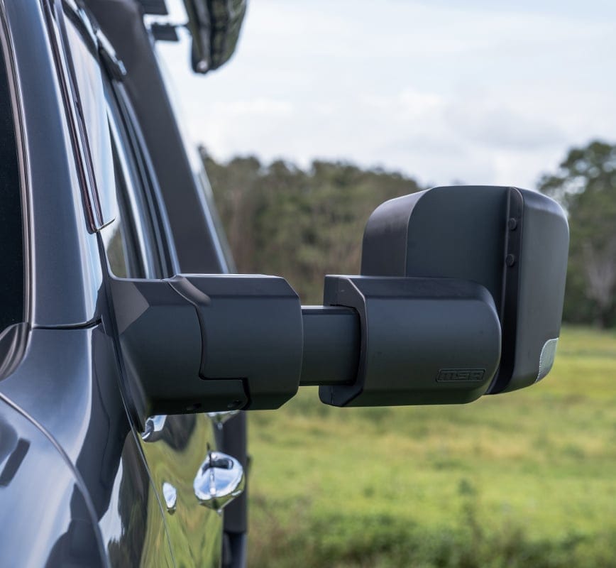 Side view of a vehicle with extended towing mirrors in an outdoor setting.