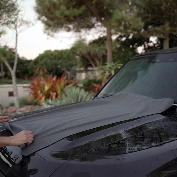 Person using Blahst Microfibre Drying Towel on a hood on a vehicle outdoors.