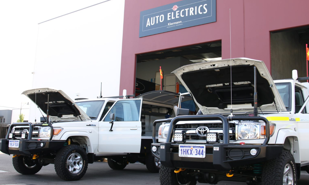 Two Toyota trucks with bonnets lifted in front of a building