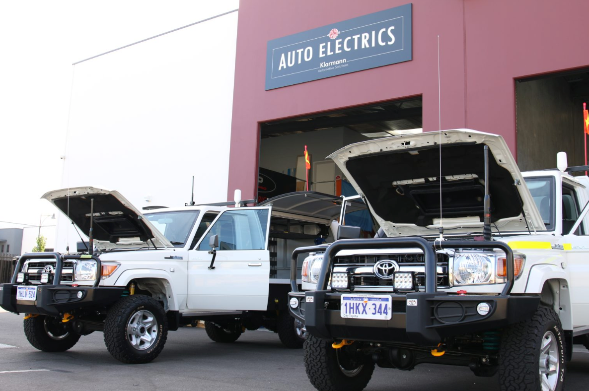Two Toyota trucks with bonnets lifted in front of a building
