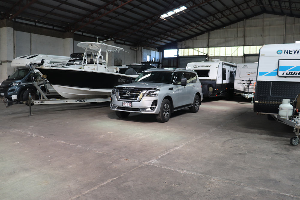 Car parked in a warehouse with boats and trailers in the background