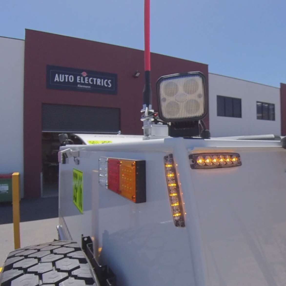 Top of a truck showing lights and a spare tire with a building in the background