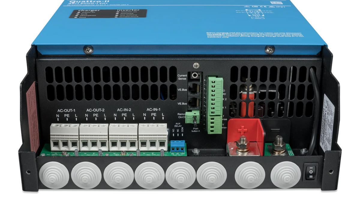 Underside connection bay of a Victron Quattro-II with the cover removed, showing the AC-IN-1, AC-IN-2, AC-OUT-1 and AC-OUT-2 terminal blocks, the VE.Bus sockets and the red and black battery studs
