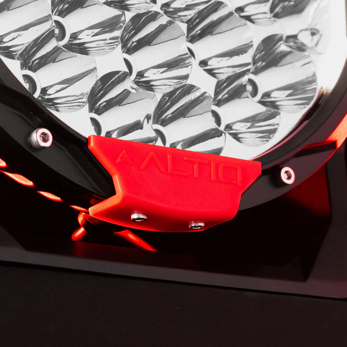 Close-up of the red ALTIQ trim tab clipped to the base of a Rogue light, with the chrome reflector cups above it and the mounting foot below