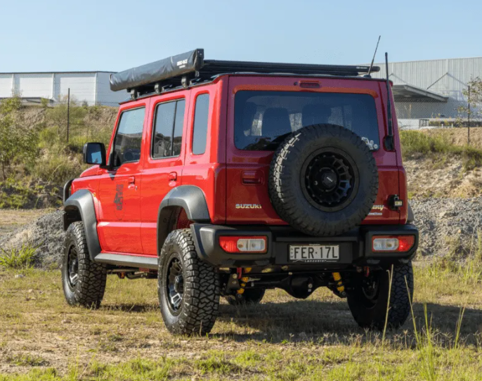 Red Suzuki truck with off-road tires and roof rack in a natural setting