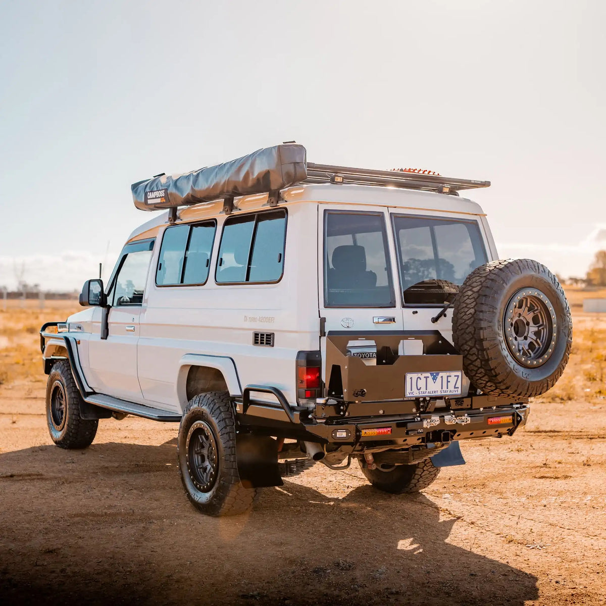 White off-road vehicle with roof rack and spare tire on a desert landscape