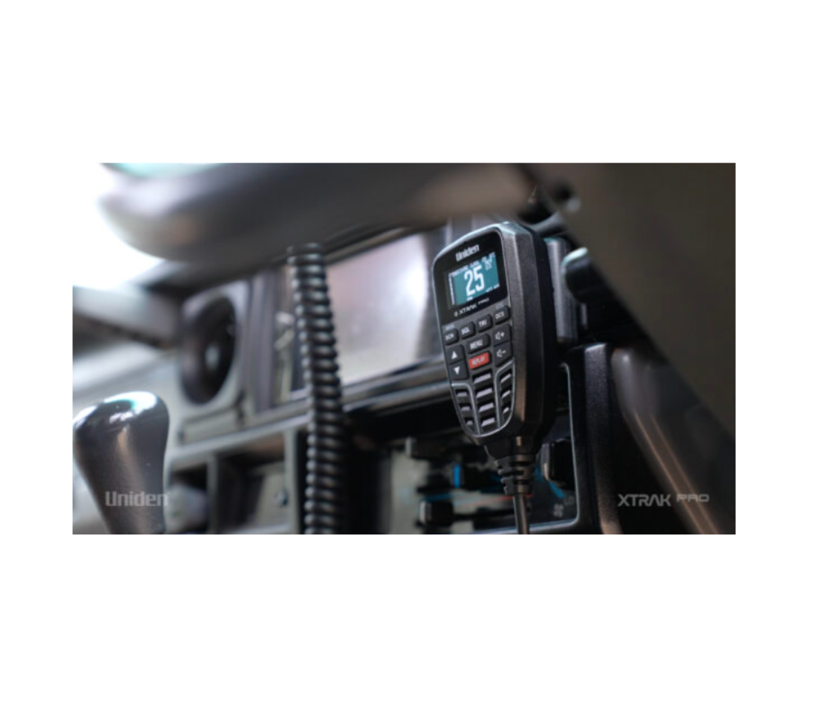 A Uniden XTRAK Pro UHF controller mounted in a vehicle cab, the backlit screen showing channel 25, with the coiled microphone lead running down beside the dash