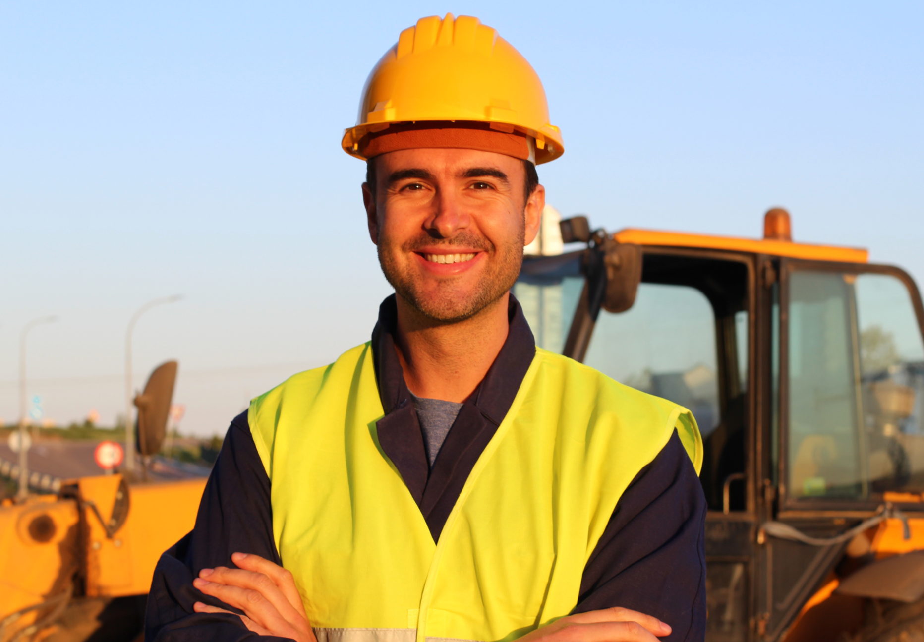 Man wearing a yellow hard hat and safety vest standing in front of construction equipment.