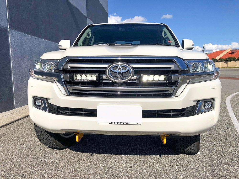 White Toyota 200 series parked on a street with a building in the background with Lazer Lamps Grille Kit – Toyota Land Cruiser 200 Series (2015–2021)