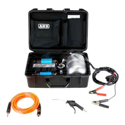 ARB twin piston compressor in its black travel case with the lid open, the twin blue cylinders and polished air tank inside, with the orange hose, blower gun and battery clamp leads laid out in front
