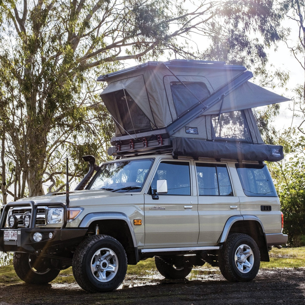 Bush Company TX27 hardshell rooftop tent open on a Land Cruiser wagon with the rainfly out, beside a lake