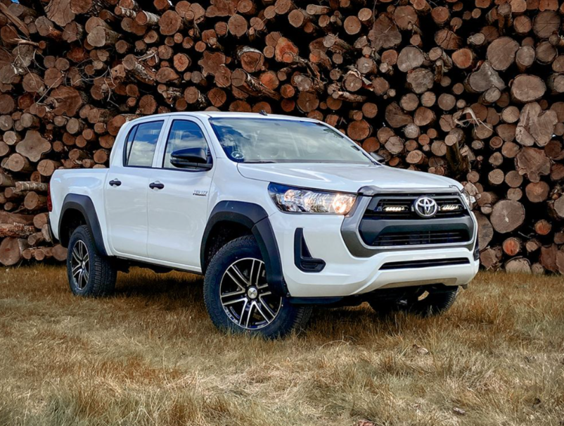 White Toyota truck parked in front of a stack of wooden logs with Lazer Lamps Grille Kit – Toyota Hilux (2021+)