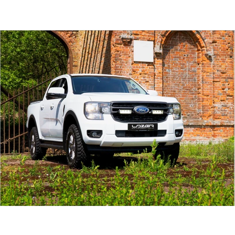 White Ford Lazer truck parked in front of a brick wall with greenery.