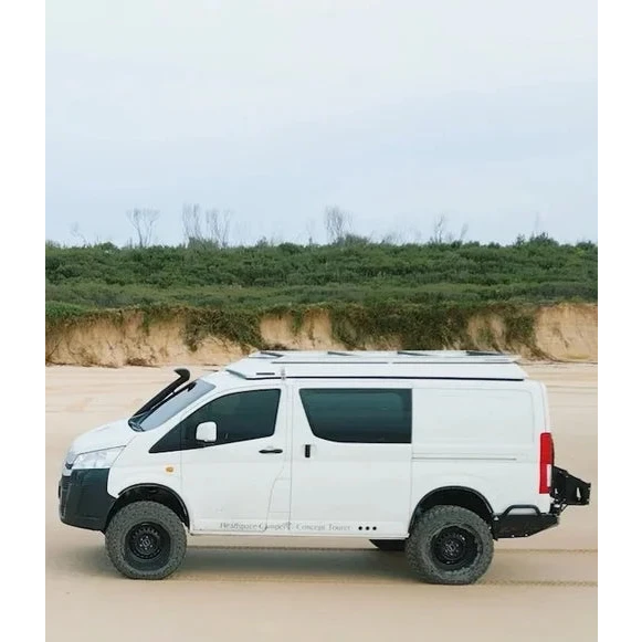 White van modified for off-road use on a sandy terrain with greenery in the background – Headspace Roof Conversion HiAce
