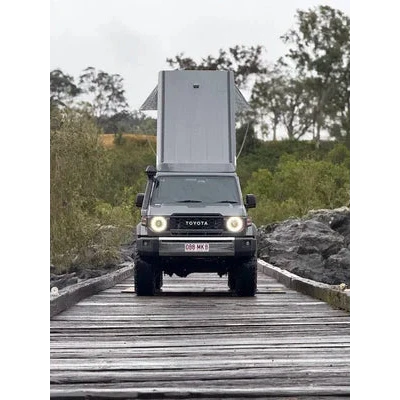 Toyota truck with a camper shell on a wooden bridge in a natural setting – Headspace Roof Conversion LC76