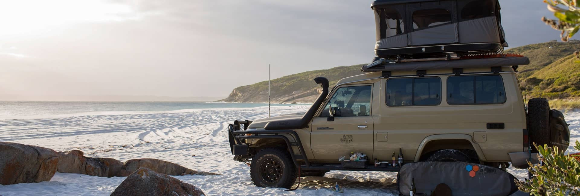 Toyota Landcruiser with camping canopy installed parked on sand beach overlooking the ocean