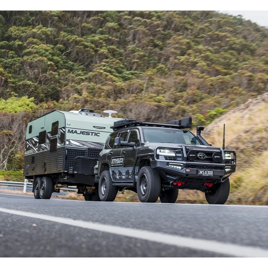 Black SUV towing a green camper trailer on a road with a mountainous background