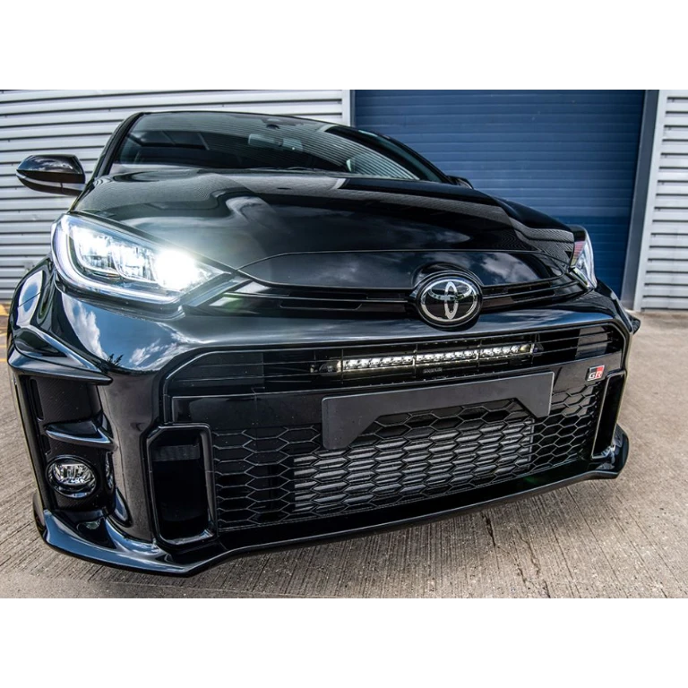 Black Toyota car with a prominent grille and headlights in front of a garage door.