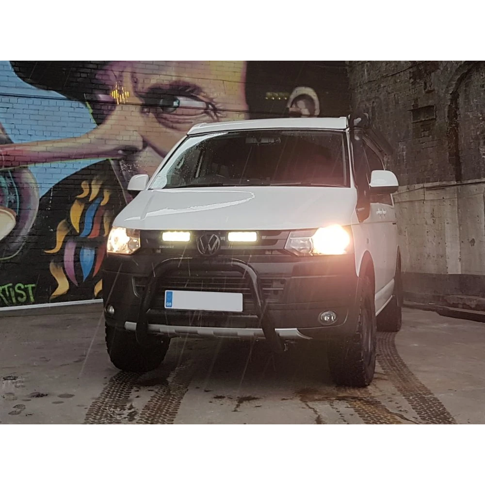 White Volkswagen van with headlights on in front of a colorful mural with Lazer Lamps Grille Kit for Volkswagen T5.1