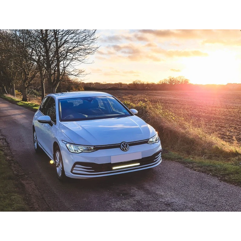 White Volkswagen car on a rural road with sunset in the background