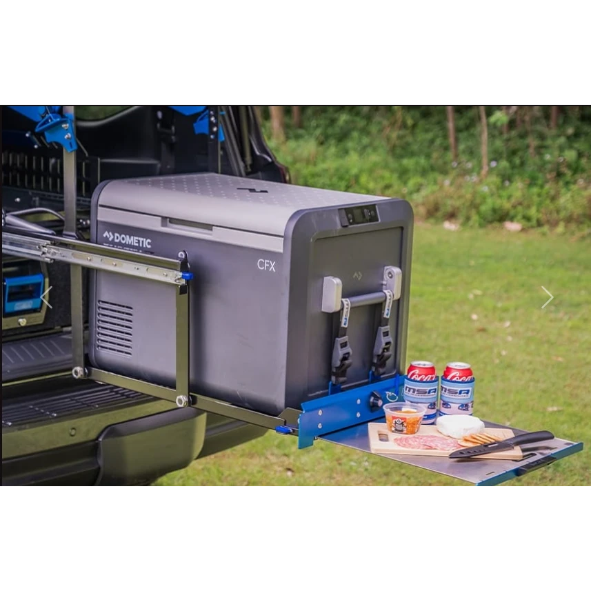 A Dometic CFX fridge strapped to an MSA drop slide, pulled out of a ute canopy and dropped down, with the fold-out table beside it holding drinks, dip and a cheese board