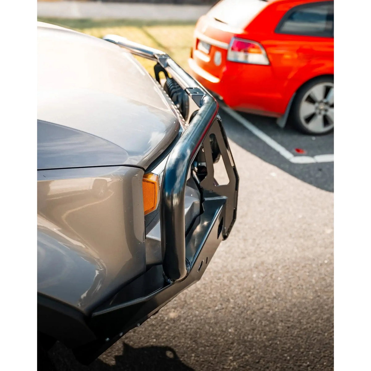 Close-up of a car bumper with another car partially visible in the background – TCC 250 Prado Bull Bar
