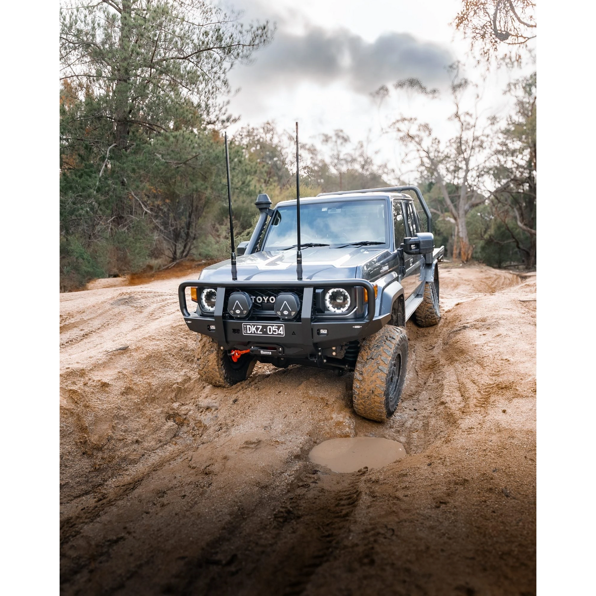 Off-road vehicle driving on a muddy path with trees in the background – TCC 70 Series Bull Bar - Facelift (2024 - Present)