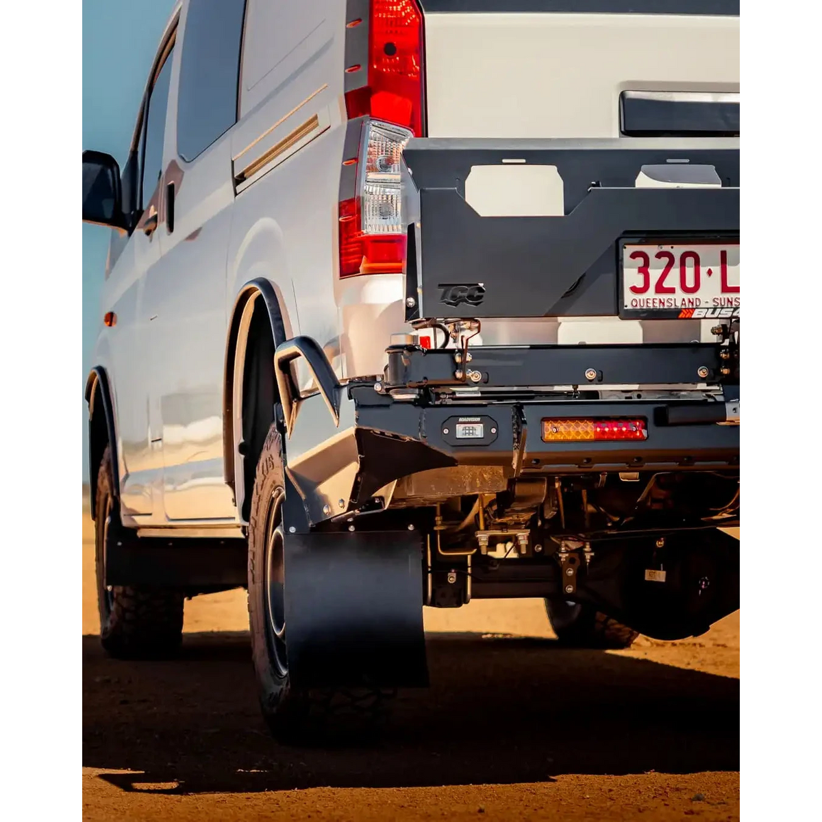 Close-up of a white van's rear with a black bumper on a dirt road – TCC Toyota Hiace 300 Series Rear Bar