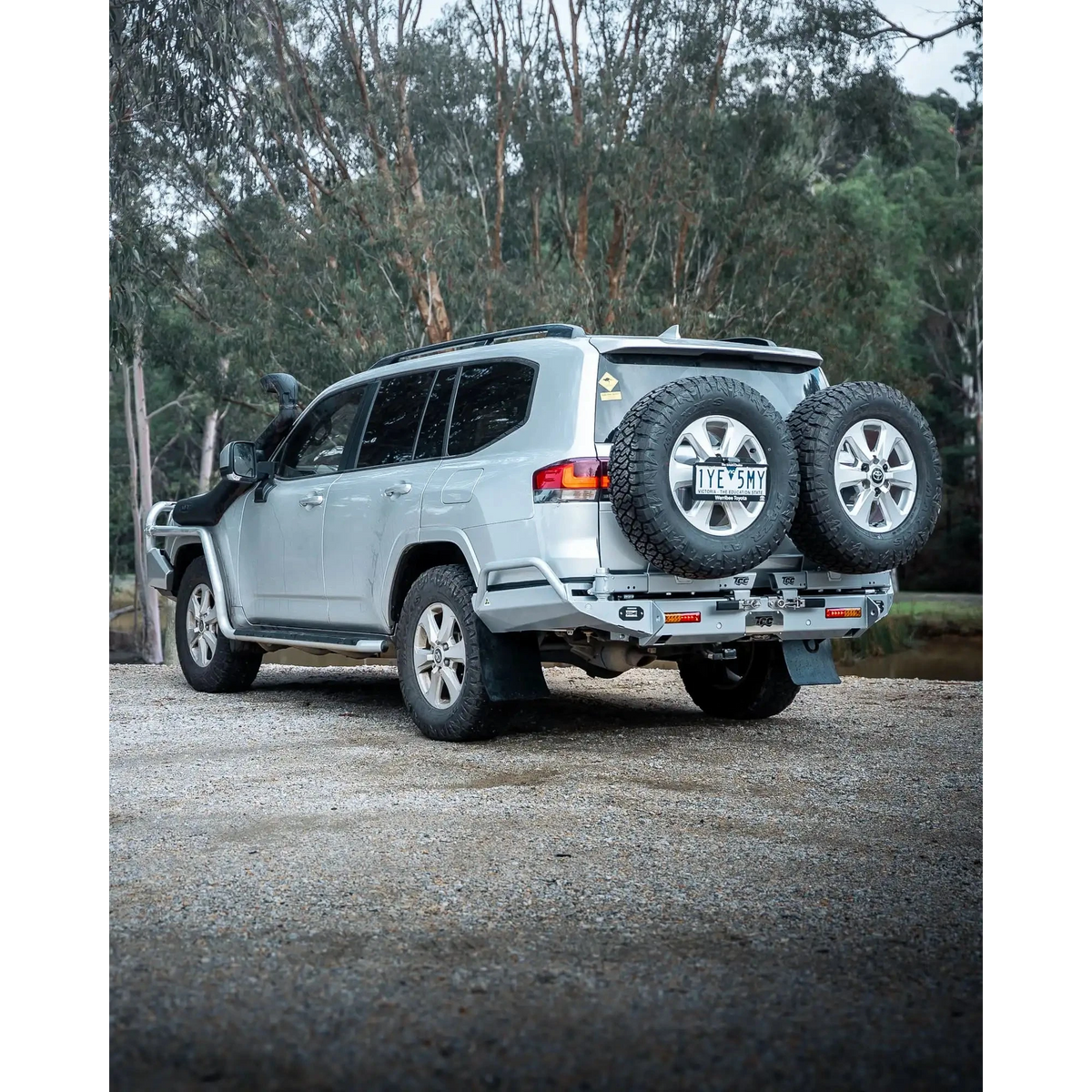 Silver SUV with spare tires on a gravel road surrounded by trees – TCC Toyota LC300 Series Rear Bar