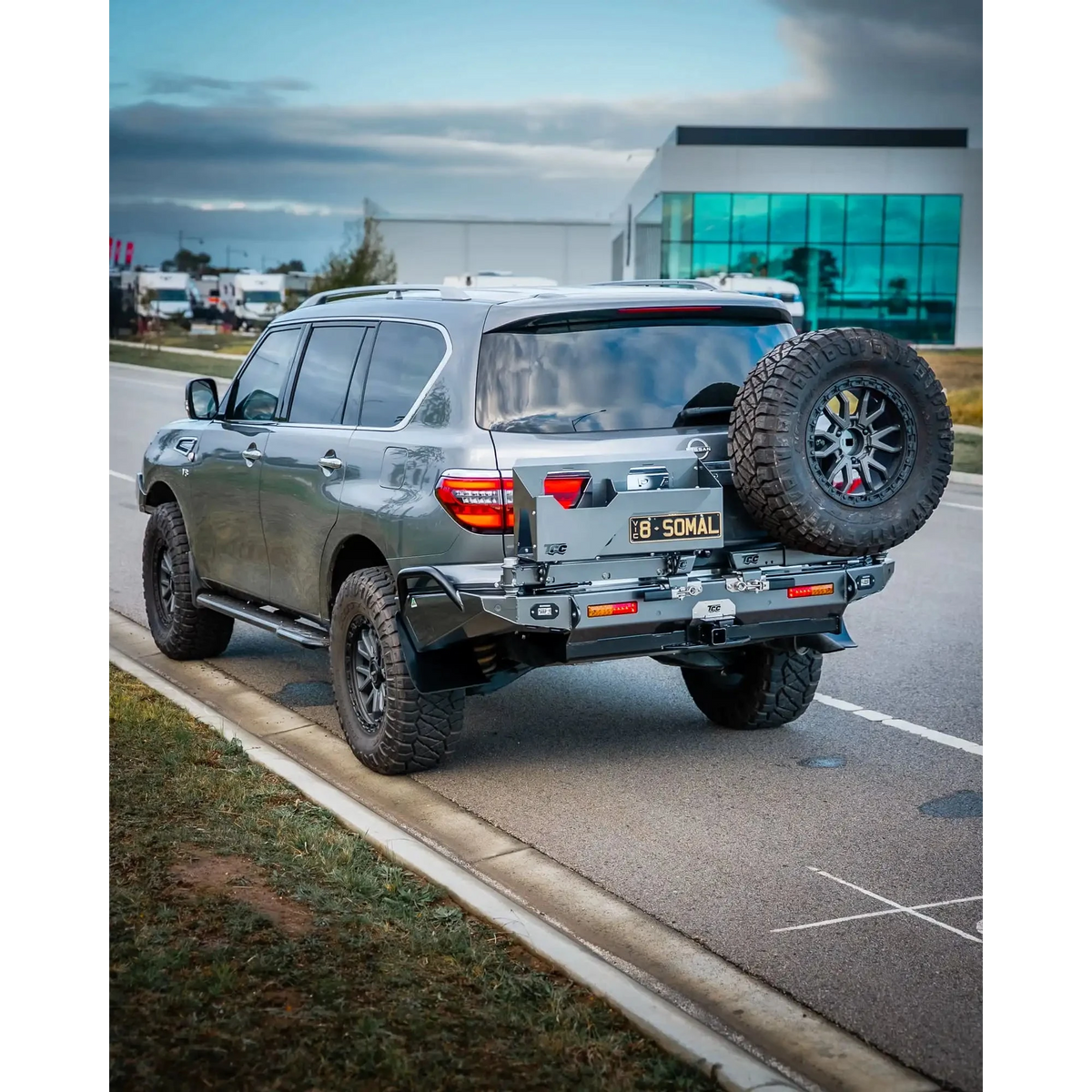 Silver SUV with off-road tires on a road near a building – TCC Y62 Patrol Rear Bar