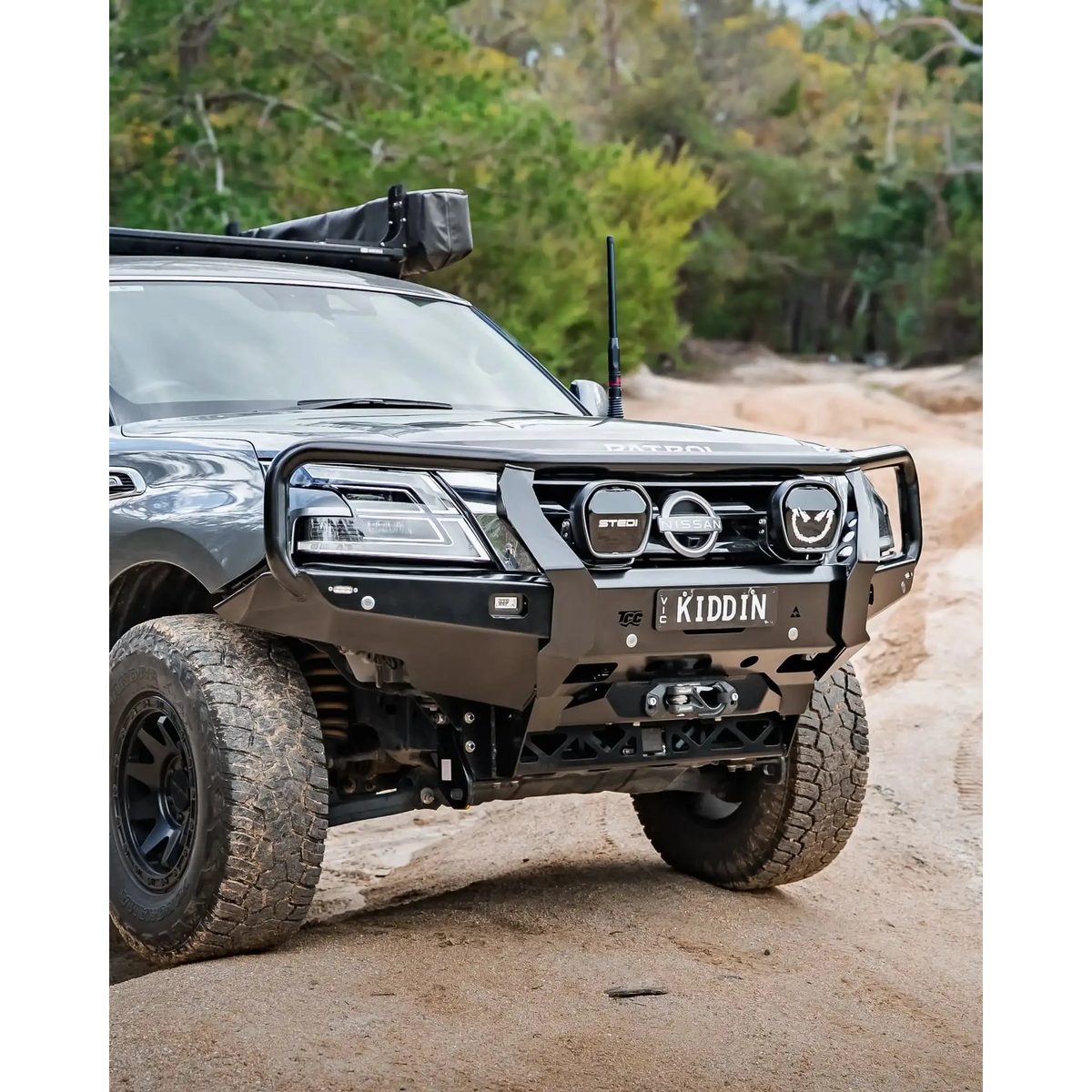 Off-road vehicle on a dirt road with trees in the background – TCC Y62 Patrol S5 Bull Bar