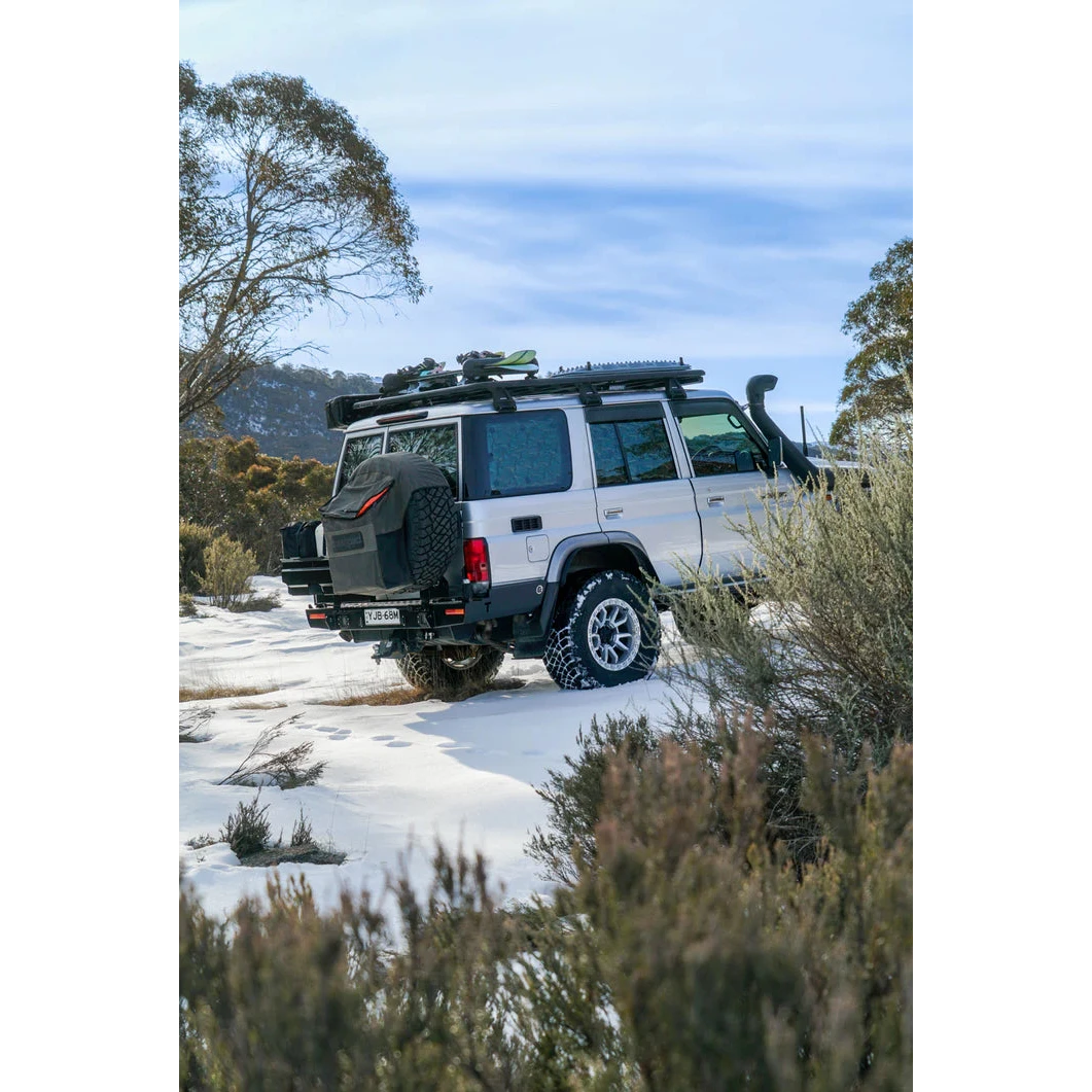4x4 vehicle on a snowy road with trees and mountains in the background – Thorburns LC76 Rear Bar