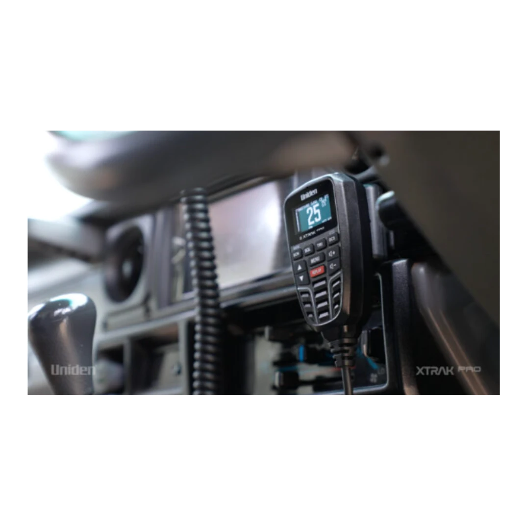 A Uniden XTRAK Pro UHF controller mounted in a vehicle cab, the backlit screen showing channel 25, with the coiled microphone lead running down beside the dash