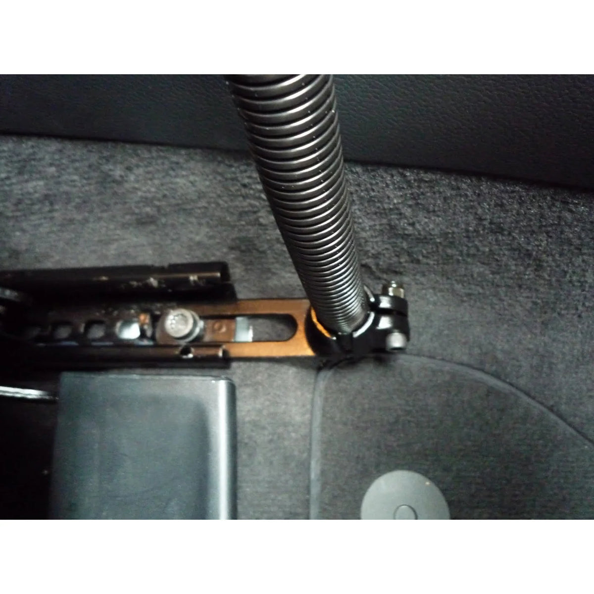 RAM floor mount installed in a vehicle footwell, the black base plate bolted through the carpet to the seat rail with the flexible aluminium rod rising from the ball clamp