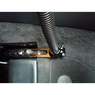 RAM floor mount installed in a vehicle footwell, the black base plate bolted through the carpet to the seat rail with the flexible aluminium rod rising from the ball clamp