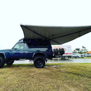 Blue SUV with a large awning extended outdoors on a grassy area.
