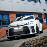White car parked in front of a building with blue windows with Lazer Lamps Bumper Beam Mount Kit for Toyota Yaris GR