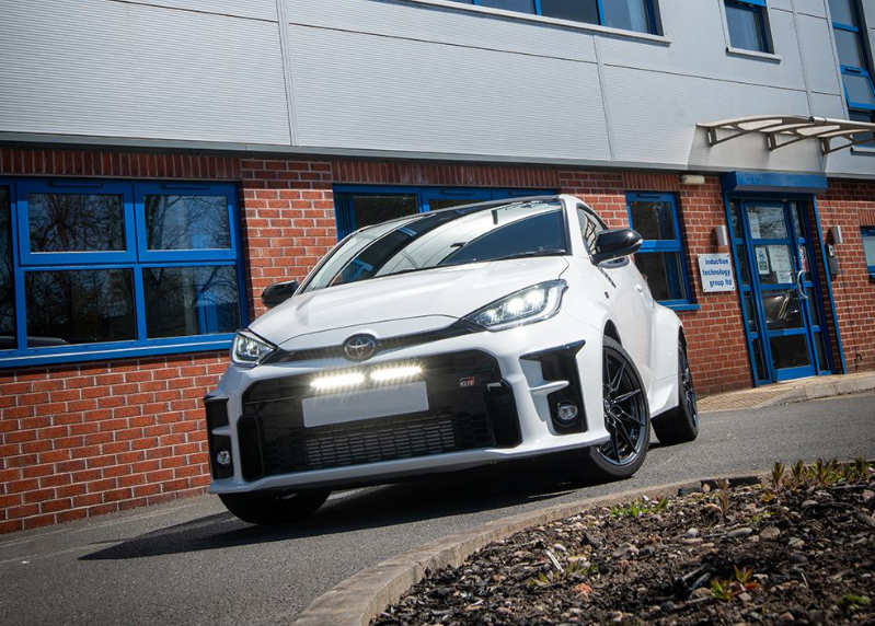 White car parked in front of a building with blue windows with Lazer Lamps Bumper Beam Mount Kit for Toyota Yaris GR