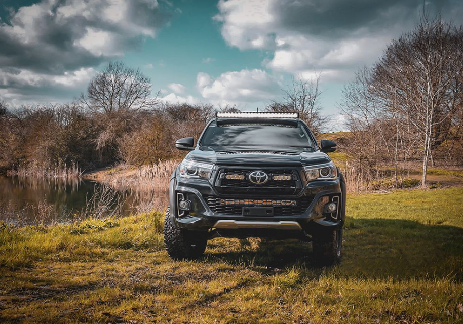 Toyota truck parked in a grassy field with trees and a lake in the background