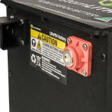 Close-up of a battery with warning labels and a red terminal on a black background