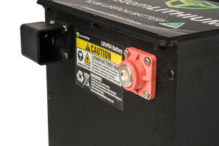 Close-up of a battery with warning labels and a red terminal on a black background