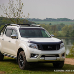 White pickup truck with roof rack parked by a lake with trees in the background