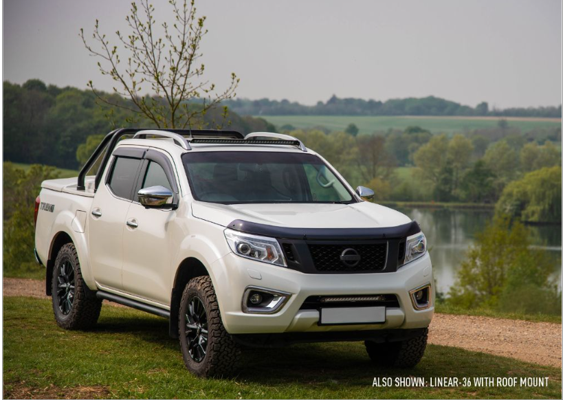 White pickup truck with roof rack parked by a lake with trees in the background