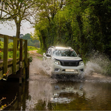 White SUV driving through a shallow stream on a forest road